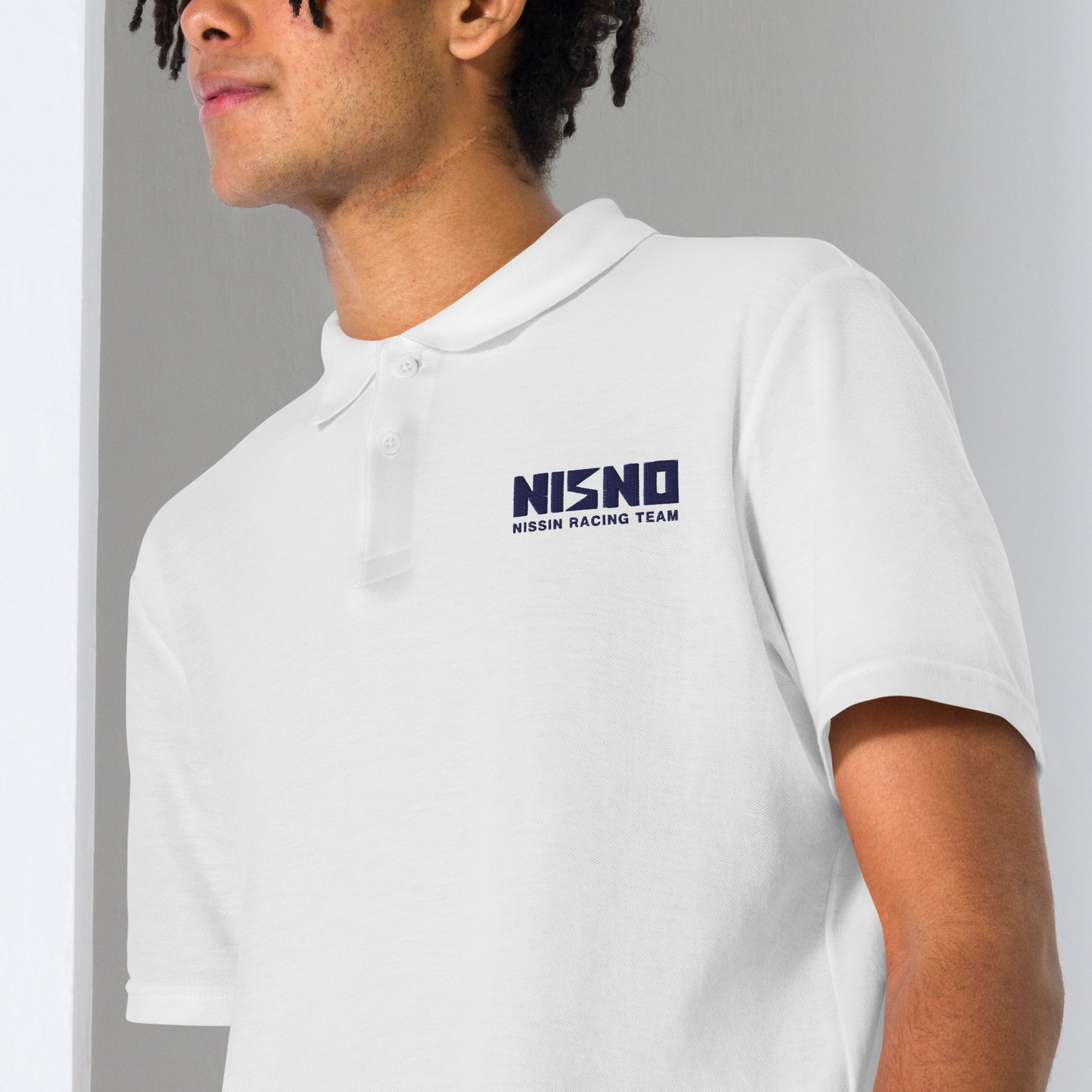 A male model wearing the 'NISNO' embroidered polo shirt in black, a replica of Iketani's shirt from Initial D. Demonstrates the relaxed fit and classic style, perfect for casual or sporty occasions.